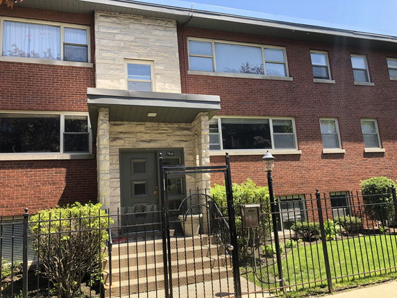 Front view of a two-story brick building with multiple windows and a gated entrance.