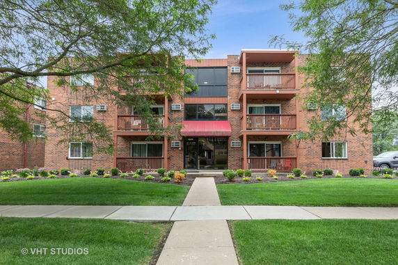 Front view of a multi-story brick apartment building with balconies and a red awning entrance.