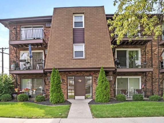 Front view of a three-story apartment building with balconies and a distinctive sloped roof.