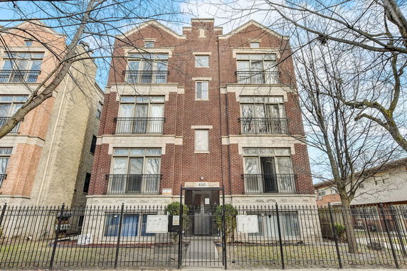 Front view of a multi-story brick building with large windows and a gated entrance.