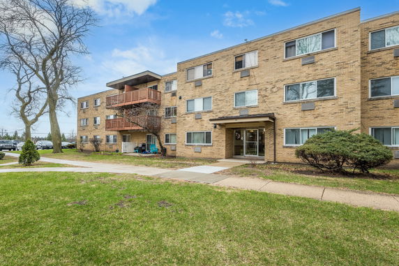 Front view of a three-story brick apartment building with balconies.