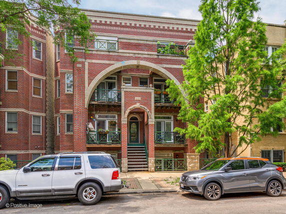 Front view of a multi-story brick building with balconies and arched entry.