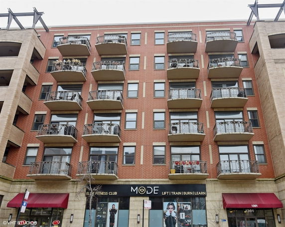 Front view of a multi-story brick building with balconies and ground-floor commercial space.