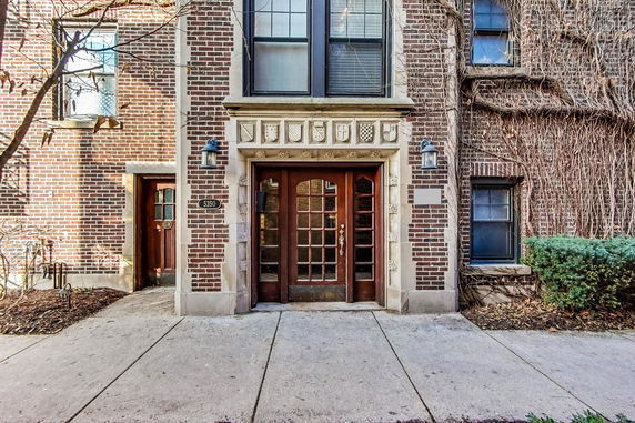 Front view of a brick building entrance with decorative stonework and wooden doors.