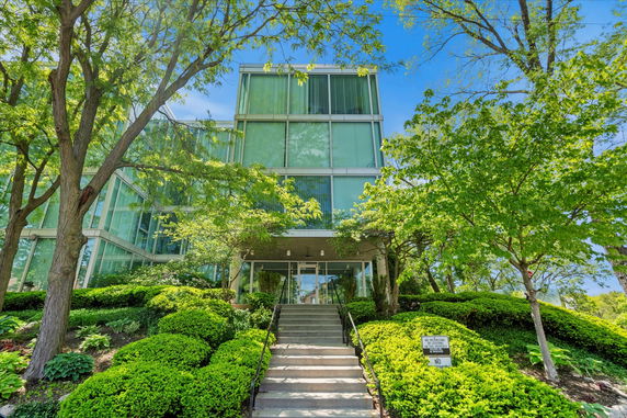 Front view of a multi-story glass building surrounded by trees and shrubs.