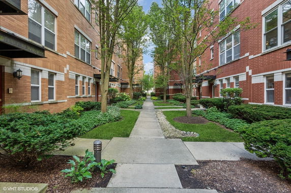 Exterior view of a multi-story brick building with landscaped walkway and greenery.