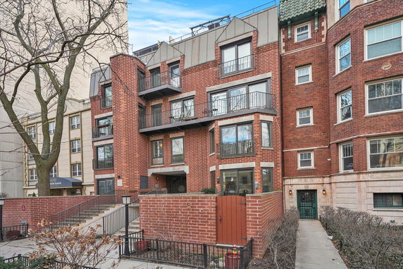 Front view of a multi-story brick building with balconies and a gated entrance.