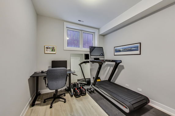 Room with a treadmill, weights, and a desk for exercise and work.