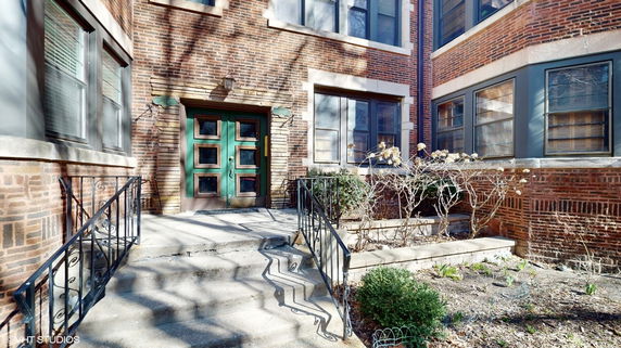 Front view of a two-story brick building with a green door and black wrought iron railings.