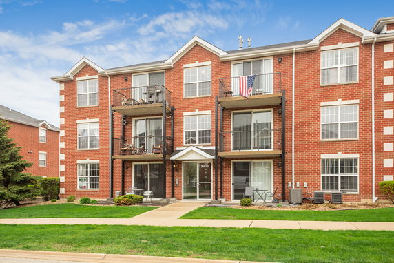 Front view of a three-story brick apartment building with balconies.