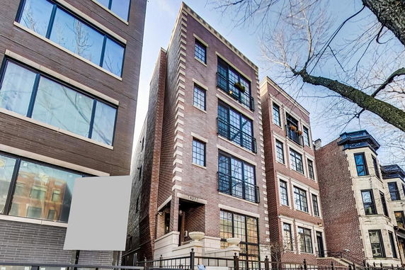 Front view of a multi-story brick building with large windows and metal railings.