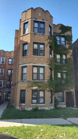 Front view of a multi-story brick apartment building with ivy on the facade.