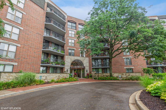 Front view of a multi-story brick apartment building with balconies and an arched entrance.