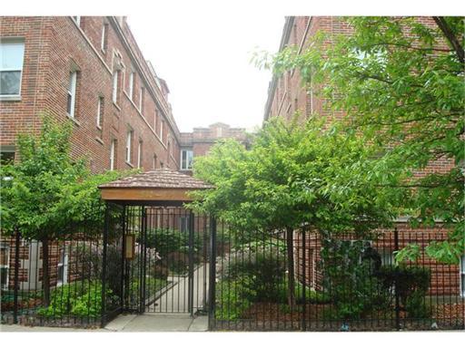 Front view of a brick multi-story building with an entrance gate and path.