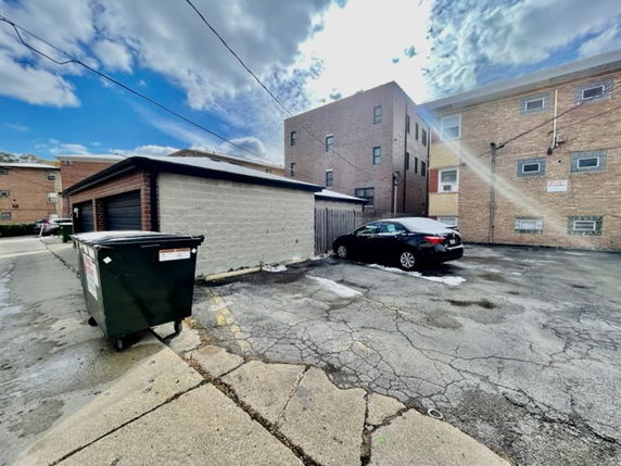 Outdoor parking area beside buildings with a car parked and a dumpster visible.