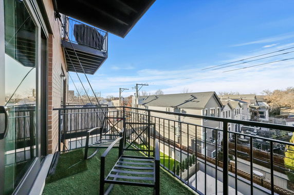 Balcony with seating and view of nearby houses and sky.
