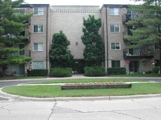 Front view of a multi-story residential building with balconies and surrounding trees.