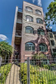 Front view of a brick multi-story apartment building with large arched windows and exterior stairs.