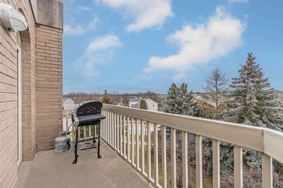 Balcony with a grill offering a view of trees and houses in the background.