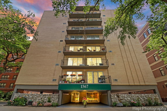 Front view of a multi-story residential building with balconies and a green entrance canopy.