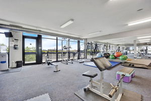 Interior view of a gym with various exercise equipment and large windows.