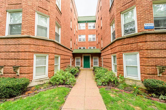Front view of a multi-story brick apartment building with a green entrance canopy.