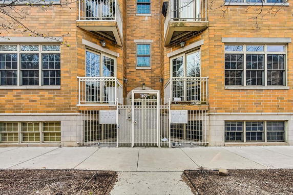 Front view of a brick multi-story building with balconies and a gated entrance.