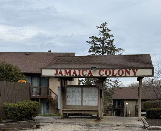 Front view of a multi-story building with a sloped roof and covered entrance area labeled 'Jamaica Colony'.