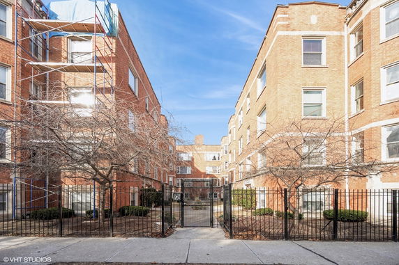 Front view of a multi-story brick apartment building with a central gated entrance.
