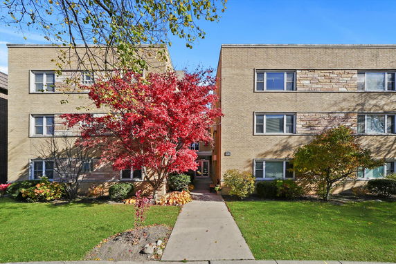 Front view of a two-story brick apartment building with large windows and a central entrance.