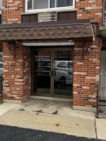 Front view of a brick building entrance with glass doors and an awning.