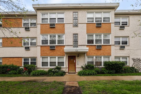 Front view of a multi-story brick apartment building with a central entrance and multiple windows.