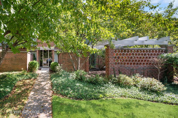 Front view of a brick house with a pathway, surrounded by greenery and trees.