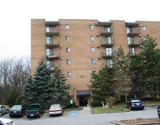 Front view of a multi-story brick apartment building with balconies and a parking area.