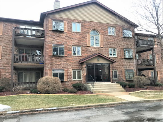 Front view of a multi-story brick apartment building with balconies and a central entrance.