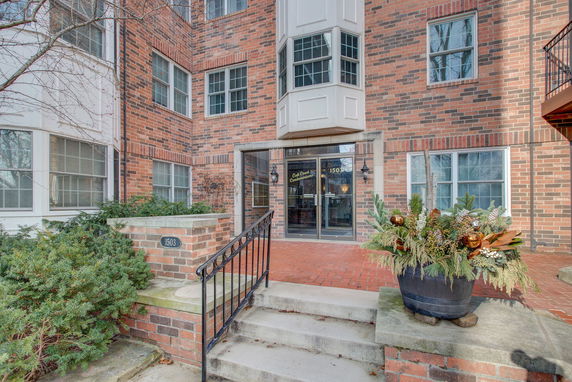 Front view of a brick condominium entrance with steps and decorative plants.