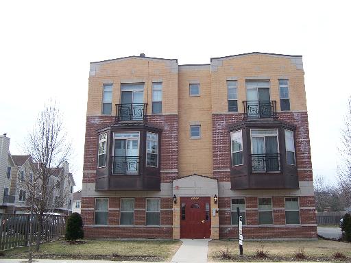 Front view of a three-story residential building with brick and yellow siding.