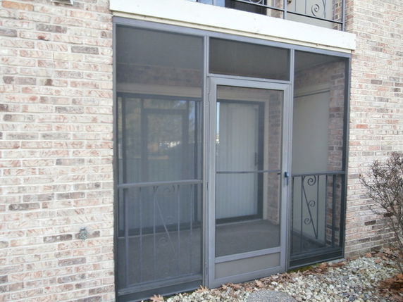 Front view of a screened-in porch attached to a brick building.
