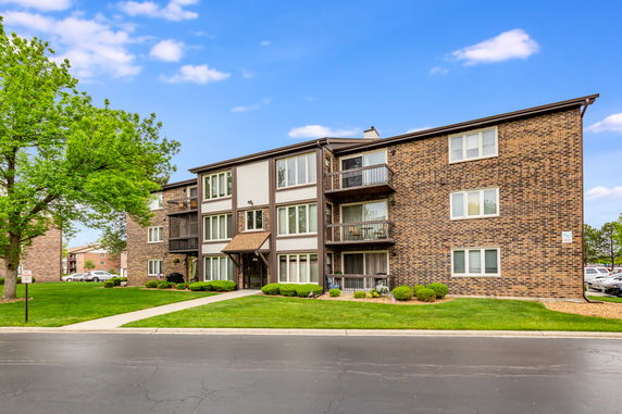 Front view of a three-story brick apartment building with a well-maintained lawn.