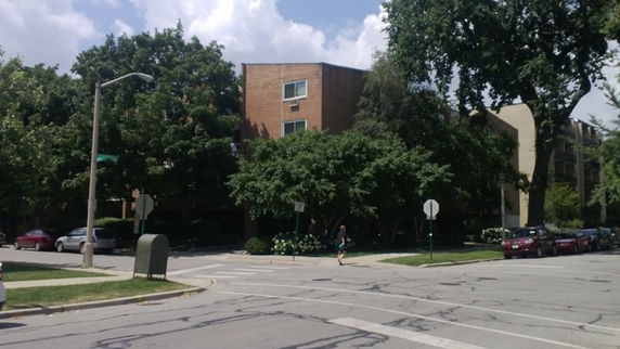 Front view of a multi-story brick building with trees and parked cars.