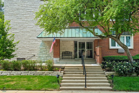 Front view of a building with stone and brick facade, entrance steps, and a metal canopy.