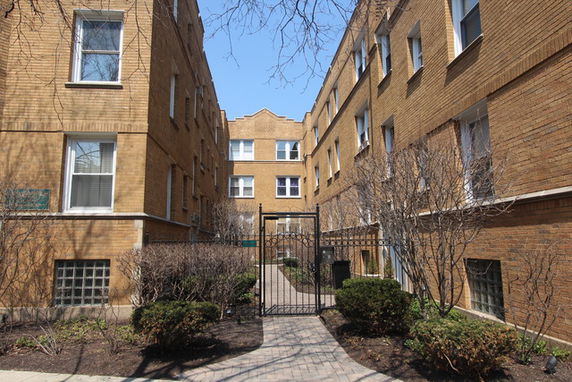 Front view of a multi-story brick apartment building with a central pathway and gate.