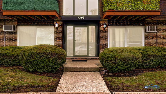 Front view of a brick building entry with an overhead address sign and landscaped bushes.