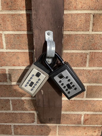 Two lockboxes attached to a wooden post on a brick wall.