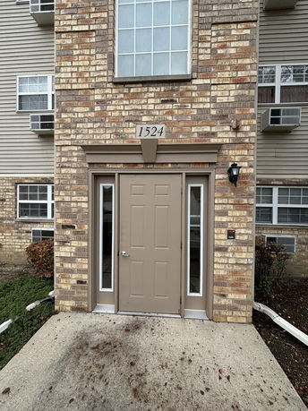 Front view of a brick building entrance with a door and a large window above.