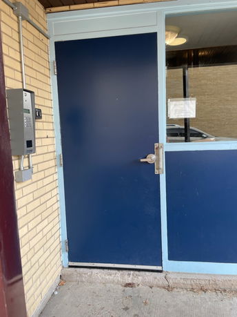 Front view of a building entrance with a blue door and intercom system.