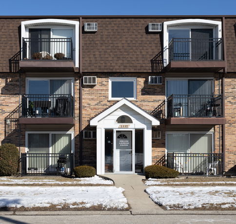 Front view of a multi-story brick apartment building with balconies and entrances.