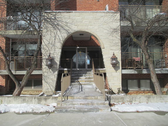 Front view of a brick apartment building with entrance archway and balconies.