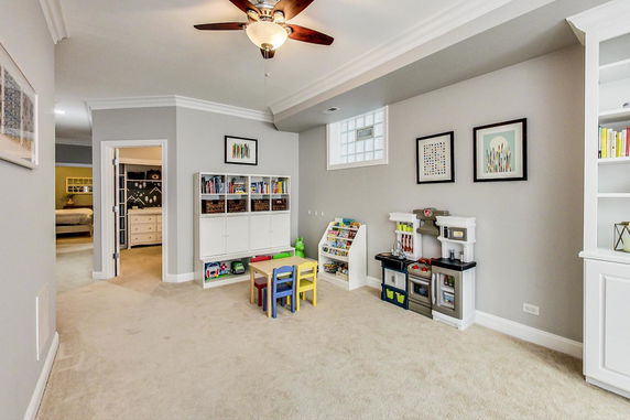 Room with children's play area, including a play kitchen set, a table with colorful chairs, and bookshelves.