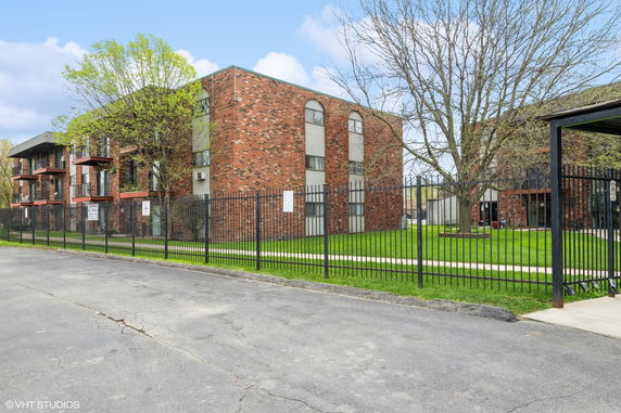 Front view of a brick apartment building with balconies and fenced lawn.